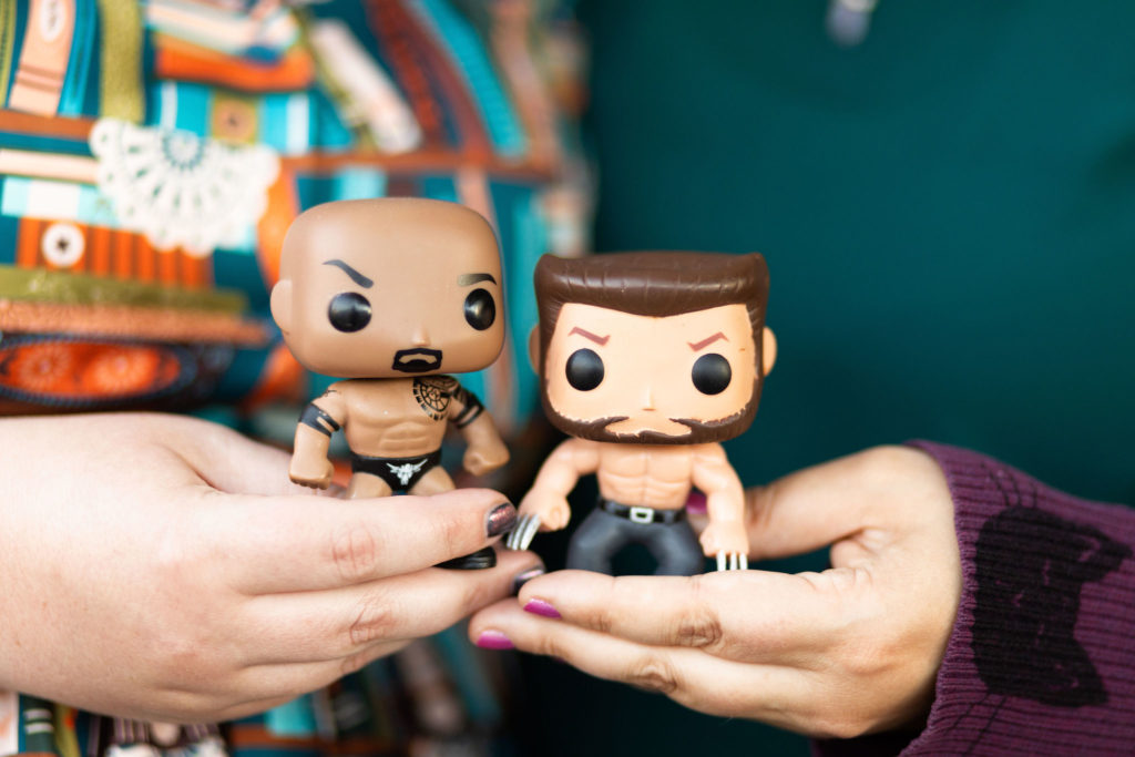 Kait and Renata's hands holding Funko Pops of The Rock and Wolverine
